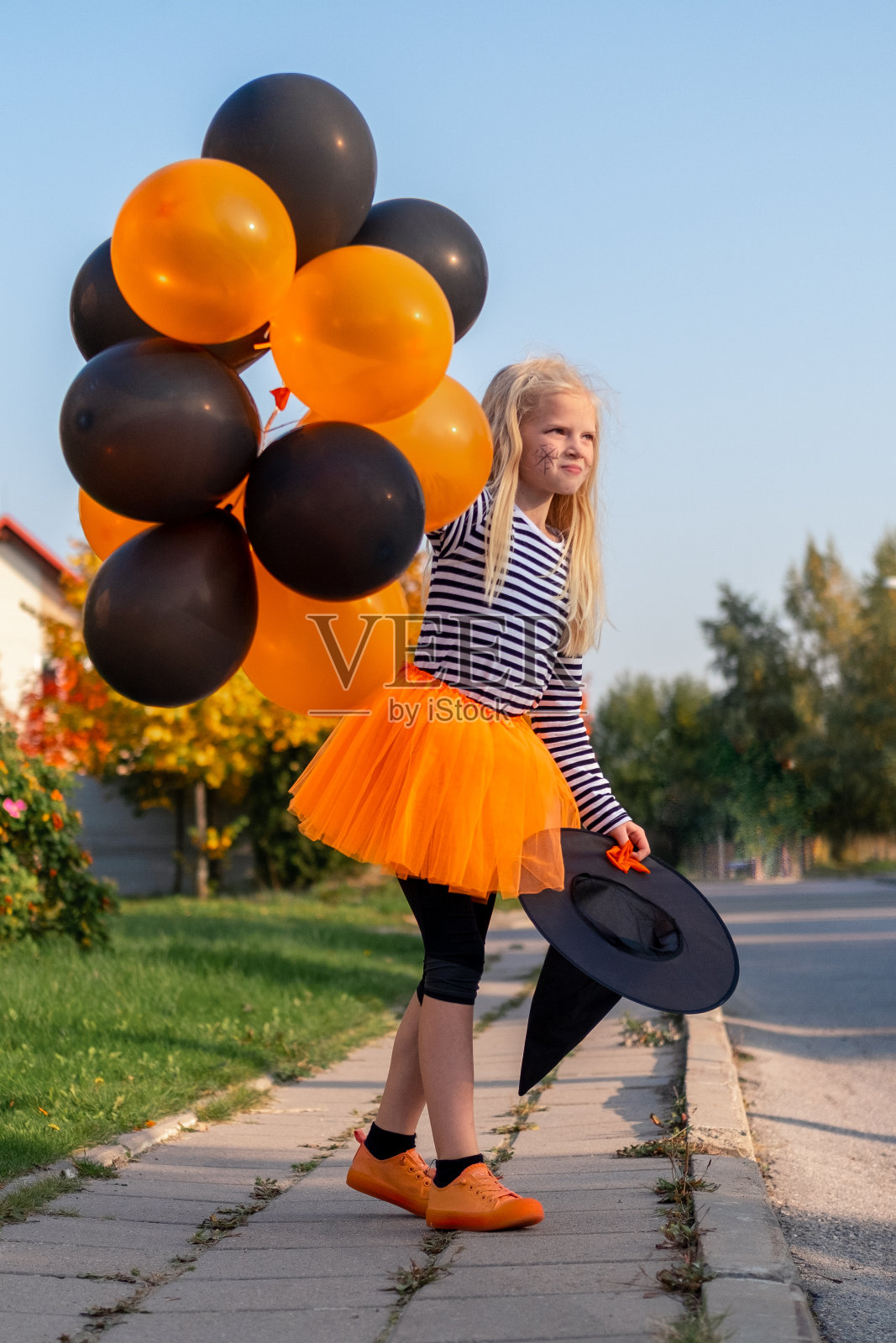 万圣节孩子们。肖像女孩戴着女巫帽和橙色和黑色的气球。在户外穿着狂欢节服装的有趣的孩子们照片摄影图片