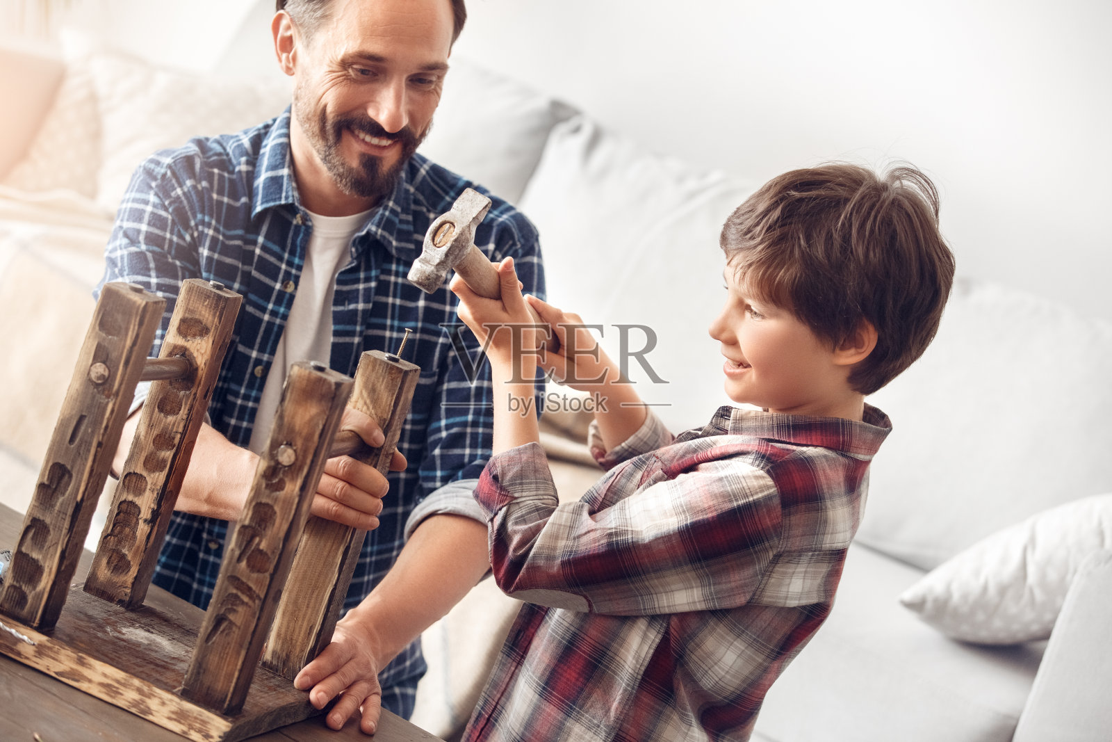 爸爸和小儿子站在家里,爸爸笑眯眯地看着小男孩聚精会神地钉钉子照片摄影图片