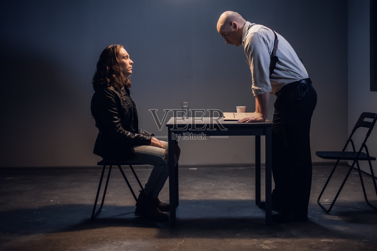 一名白人男性警探正在与一名被戴着手铐坐在审讯室里的贩毒嫌疑人交谈照片摄影图片
