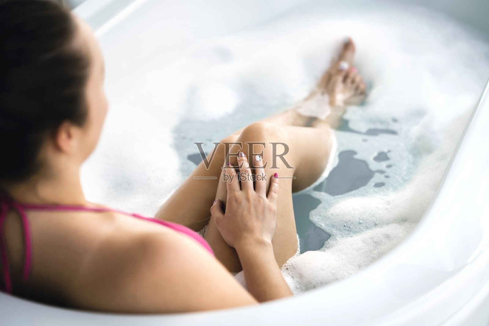 女人在洗澡。有泡泡和泡沫的浴缸。修完指甲后,用手指涂抹指甲油。清洁健康的皮肤。皮肤护理和温泉泡浴治疗。照片摄影图片