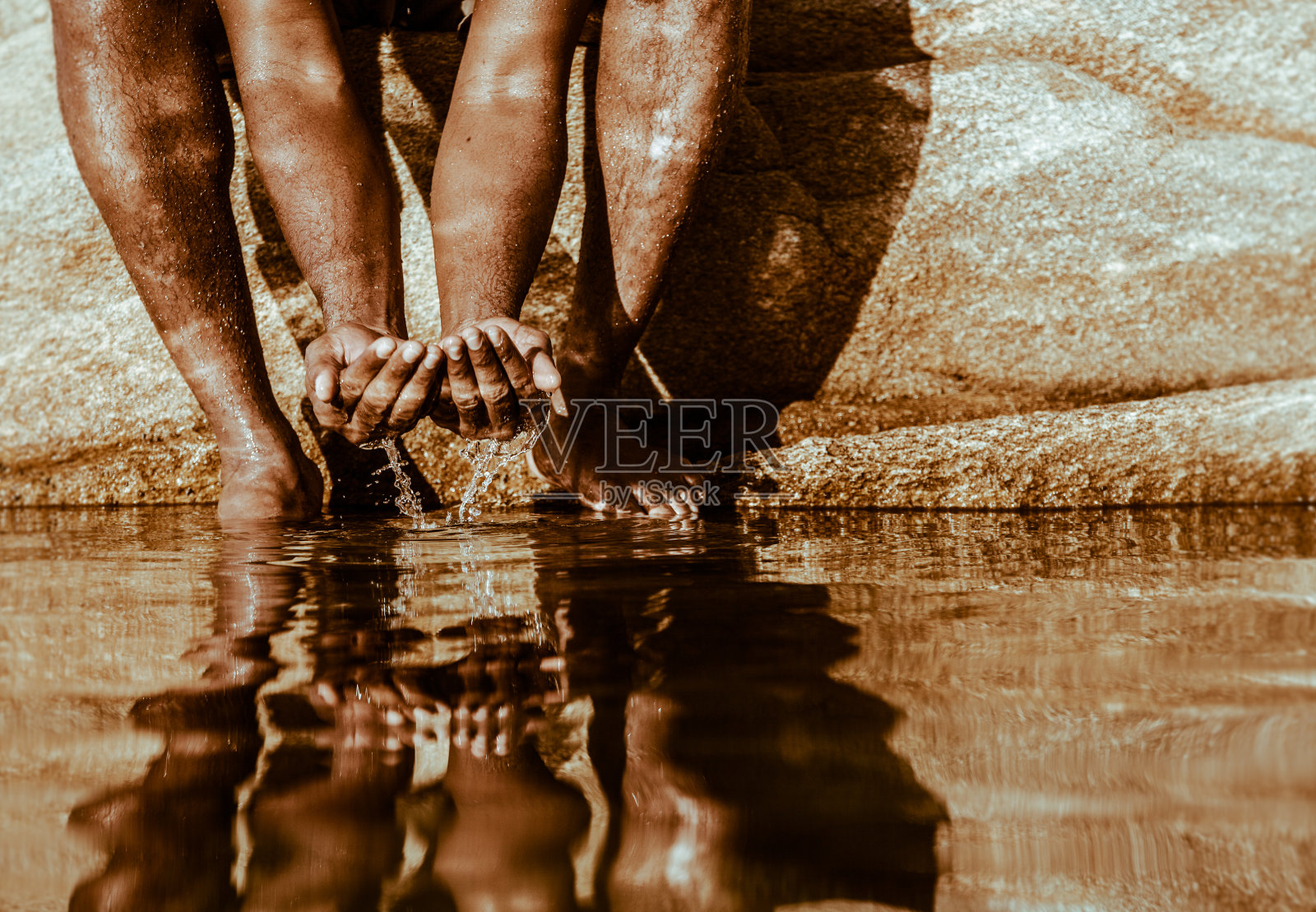 男性坐在岩石上,手捧水照片摄影图片