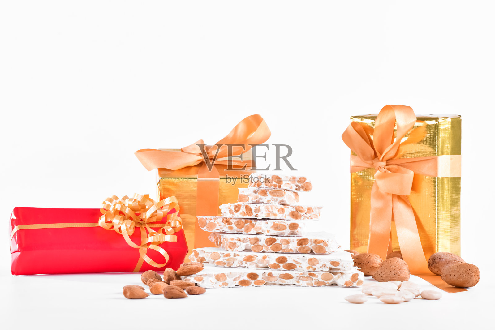 一堆牛轧糖,周围是去皮和未去皮的杏仁,后面是包装好的礼品盒,背景很亮。糖果和礼物的概念。照片摄影图片