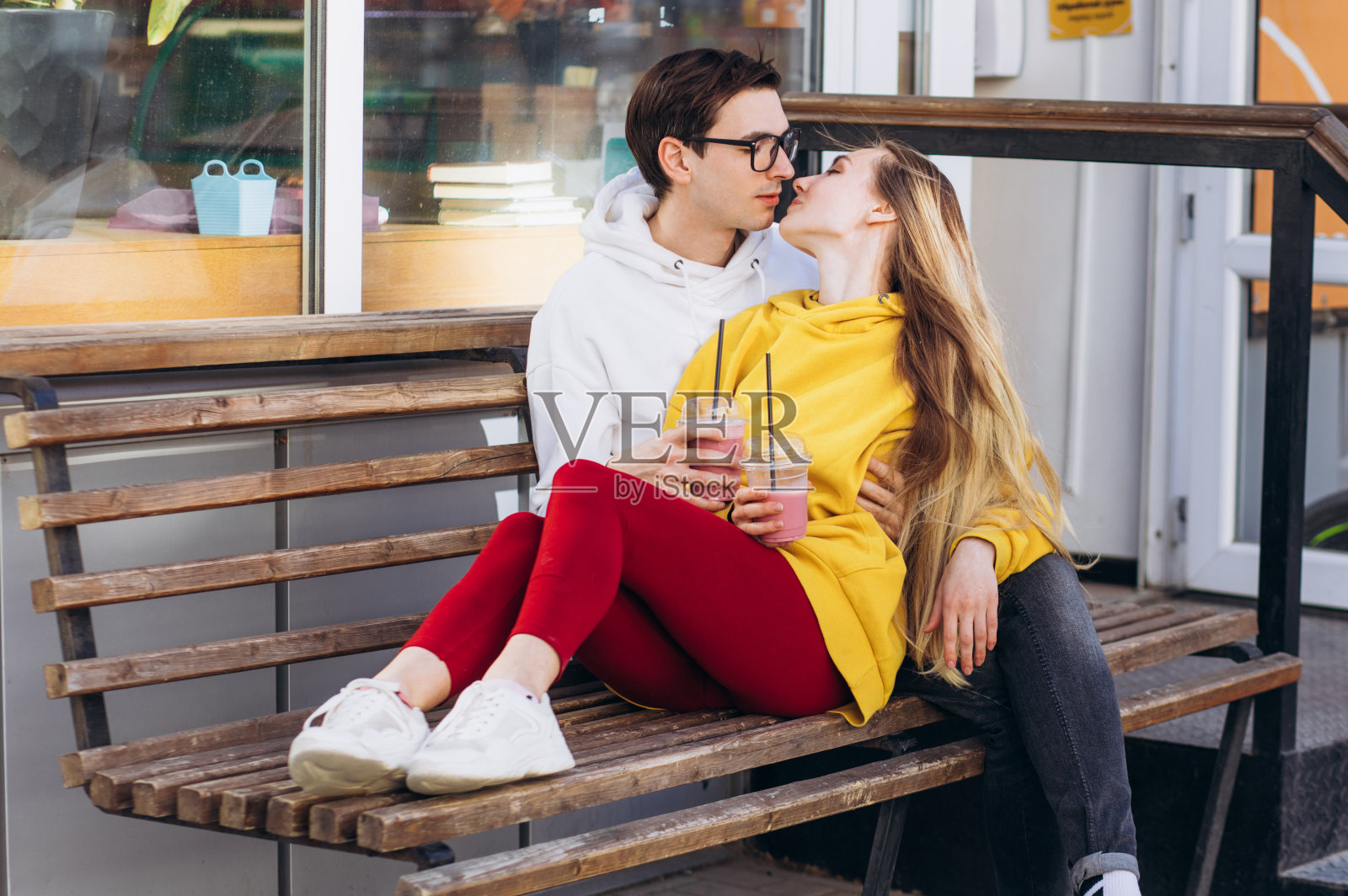 一对恩爱的情侣捧着咖啡坐在长椅上亲吻。照片摄影图片