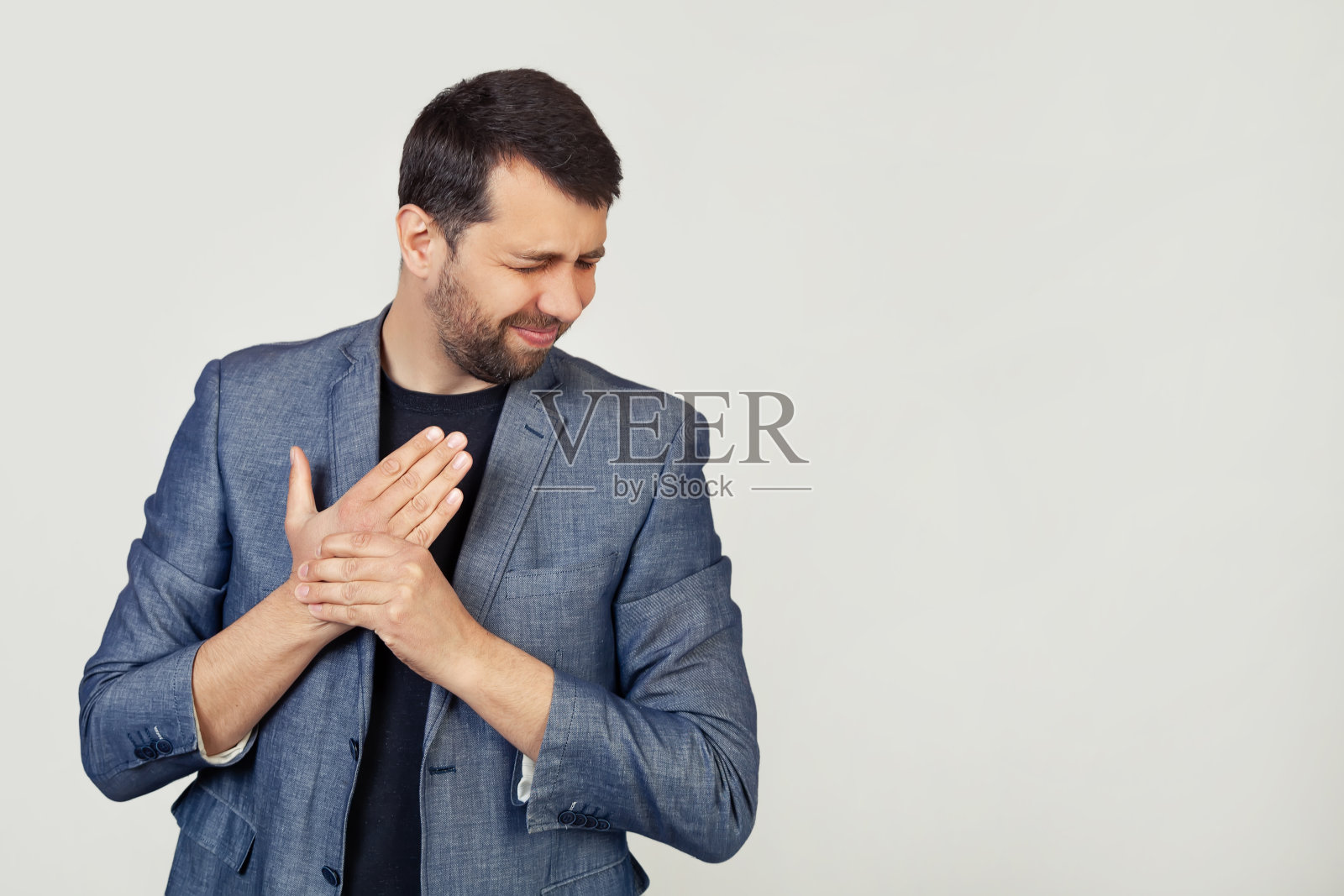 年轻的商人穿着一件留着胡子的夹克,饱受手部和手指疼痛、关节炎的折磨。灰色背景上的男子肖像照片摄影图片
