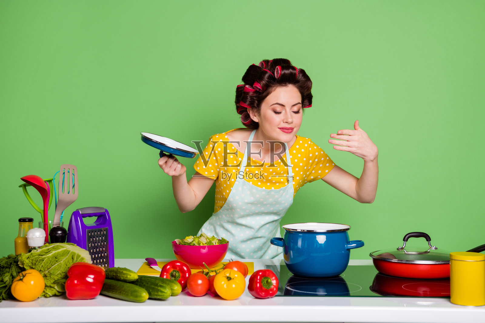 照片正面的女孩准备美味新鲜的生态汤气味芳香打开盖炖锅有番茄辣椒配料穿着黄色的斑点t恤发卷孤立的绿色背景照片摄影图片