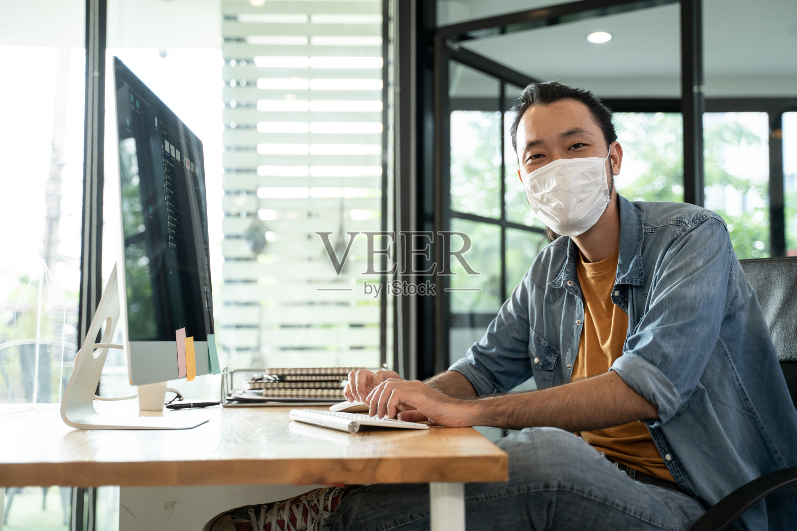 亚洲商人在办公室用电脑工作,有新的正常的生活方式概念。公司复工后,男女佩戴防护口罩,保持距离,预防新冠病毒感染。照片摄影图片