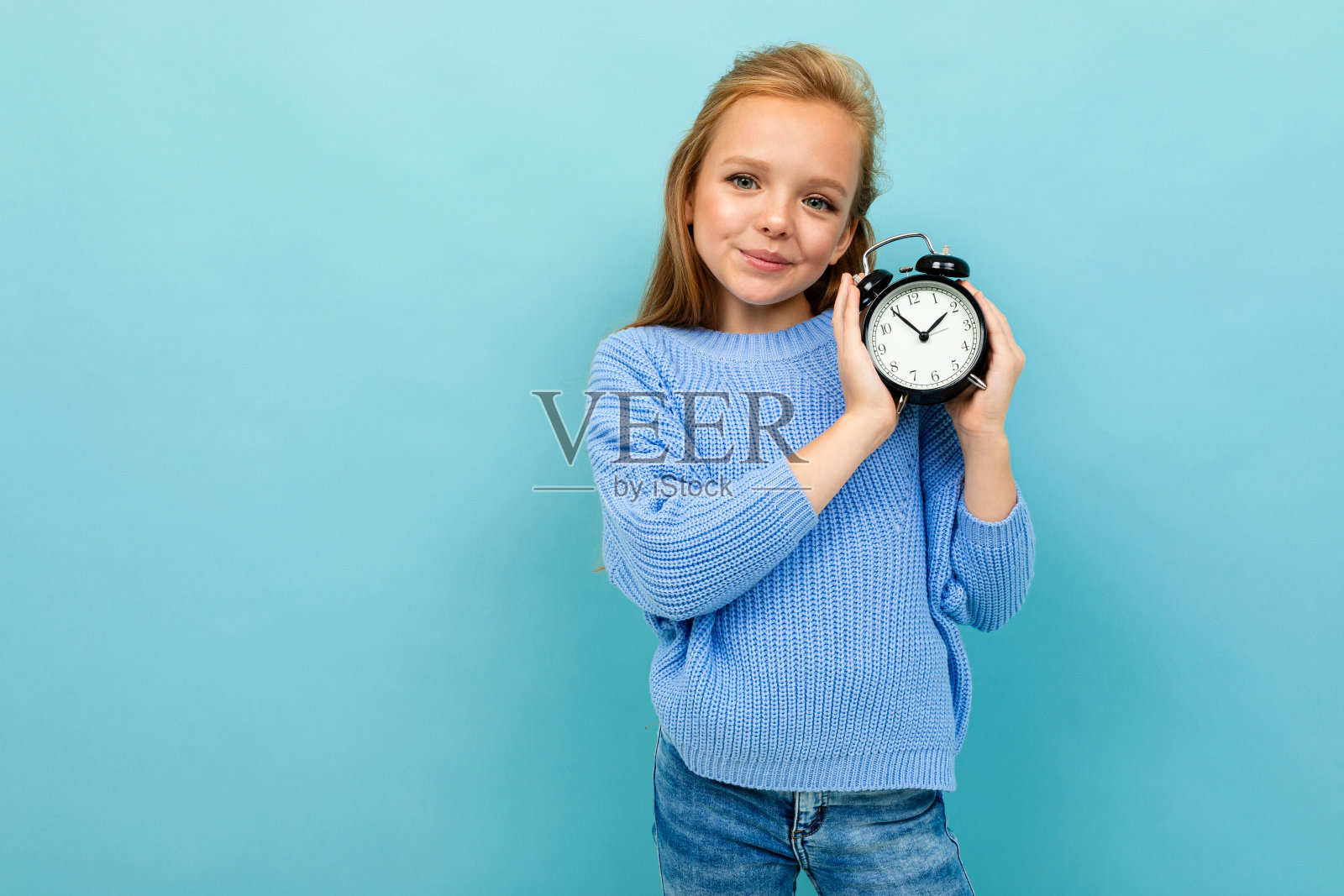 一个微笑的欧洲女孩手里拿着一个闹钟在一个浅蓝色的背景与copyspace照片摄影图片