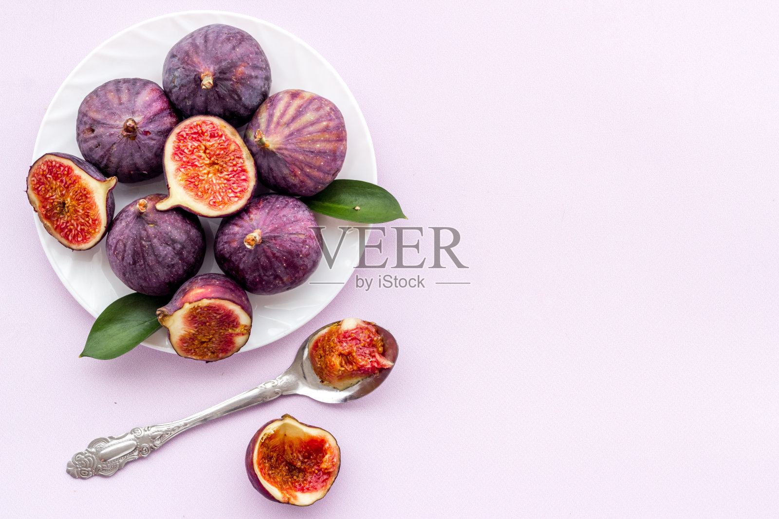 新鲜的整片无花果与绿叶一起放在盘子里。俯视图照片摄影图片