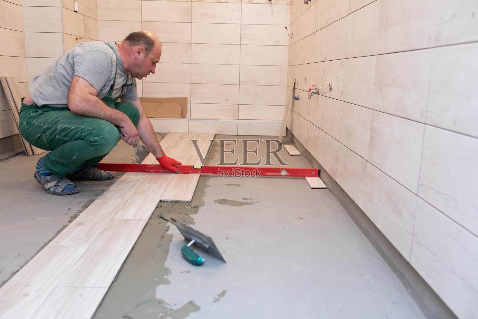 建筑工人用水平仪检查浴室地板上瓷砖的表面水平。照片摄影图片
