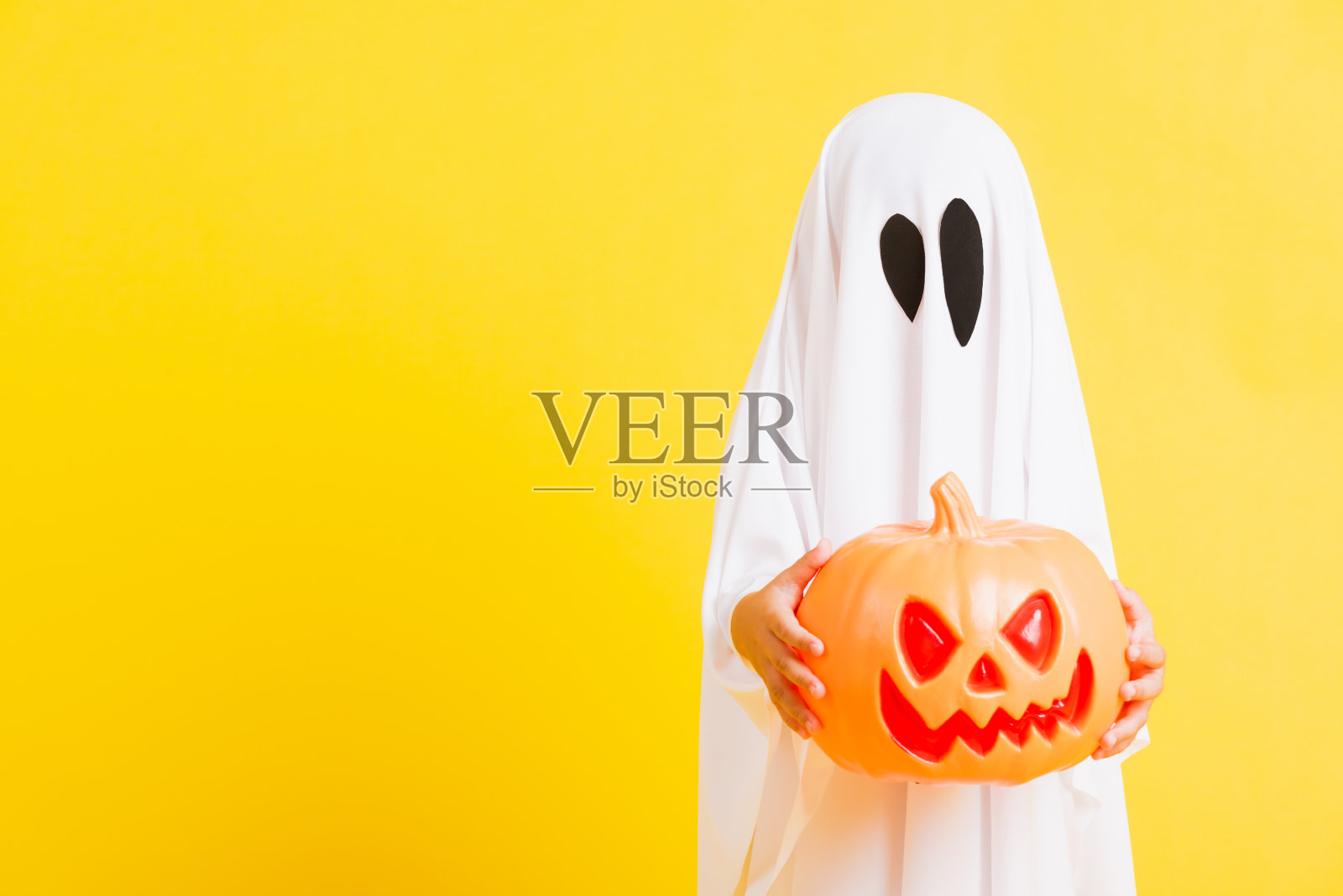 小可爱的孩子穿着白色的服装万圣节鬼吓人,他手里拿着橙色的南瓜鬼照片摄影图片