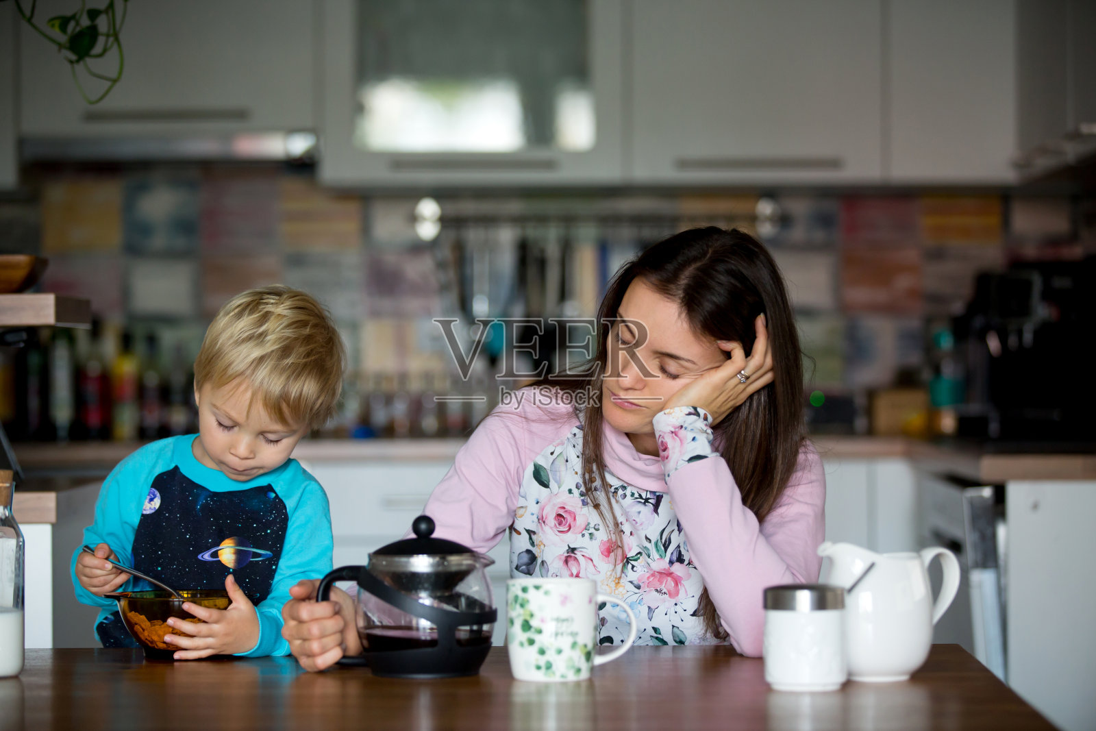 疲惫的母亲,妇女在早上喝咖啡,而孩子吃早餐照片摄影图片