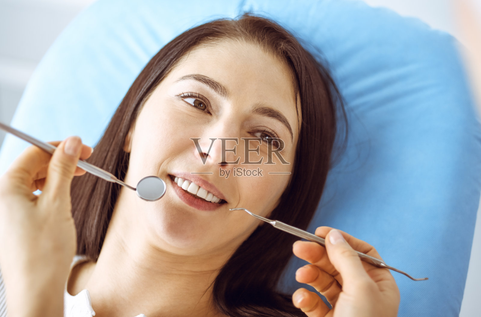 微笑的黑发女人正在检查牙医在牙科诊所。医生的手拿着牙科器械靠近病人的嘴。健康牙齿和医学理念照片摄影图片