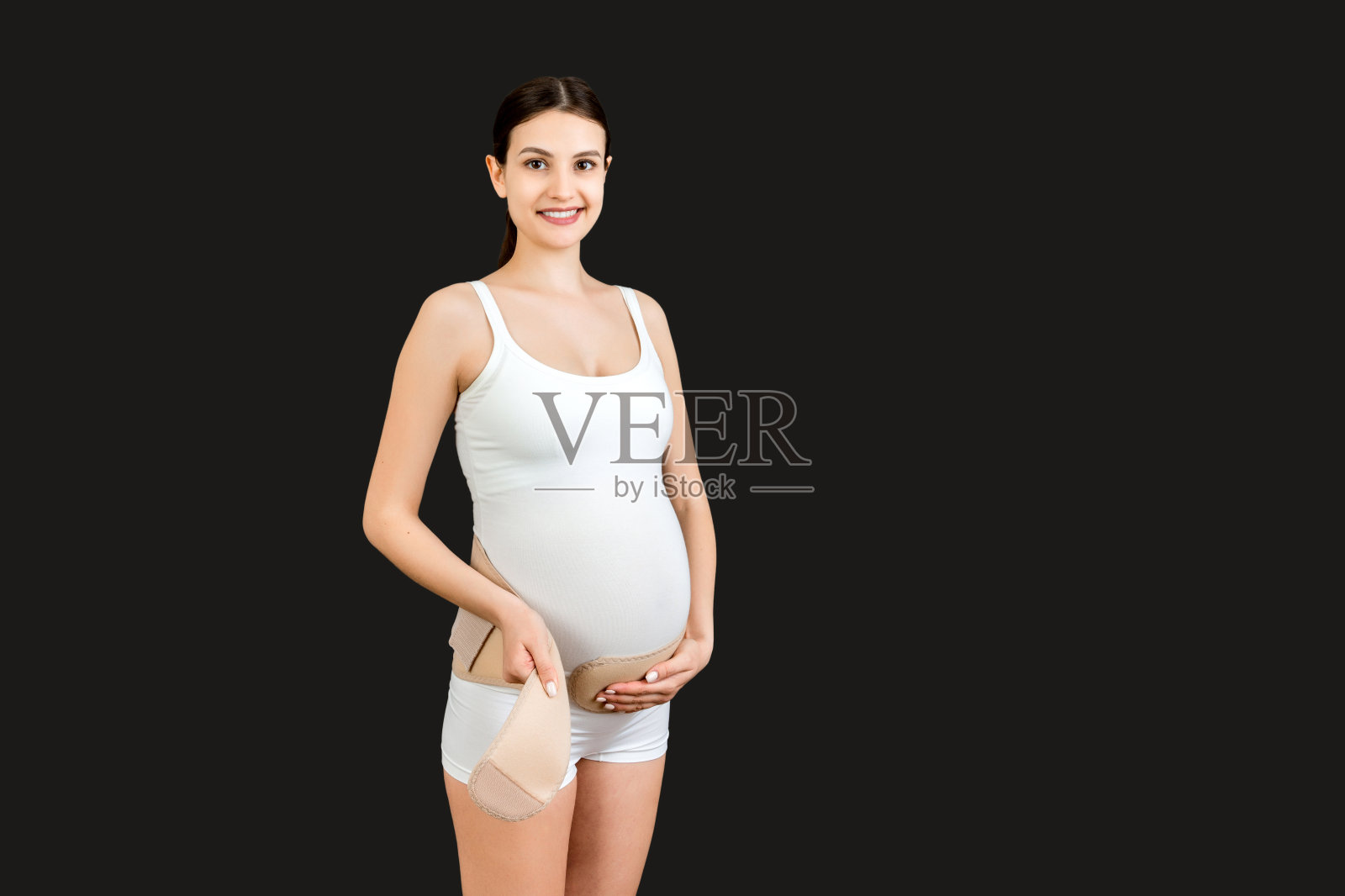 孕妇的肖像在黑色背景与复制空间上粘贴怀孕绷带。骨科腹部支撑带概念照片摄影图片