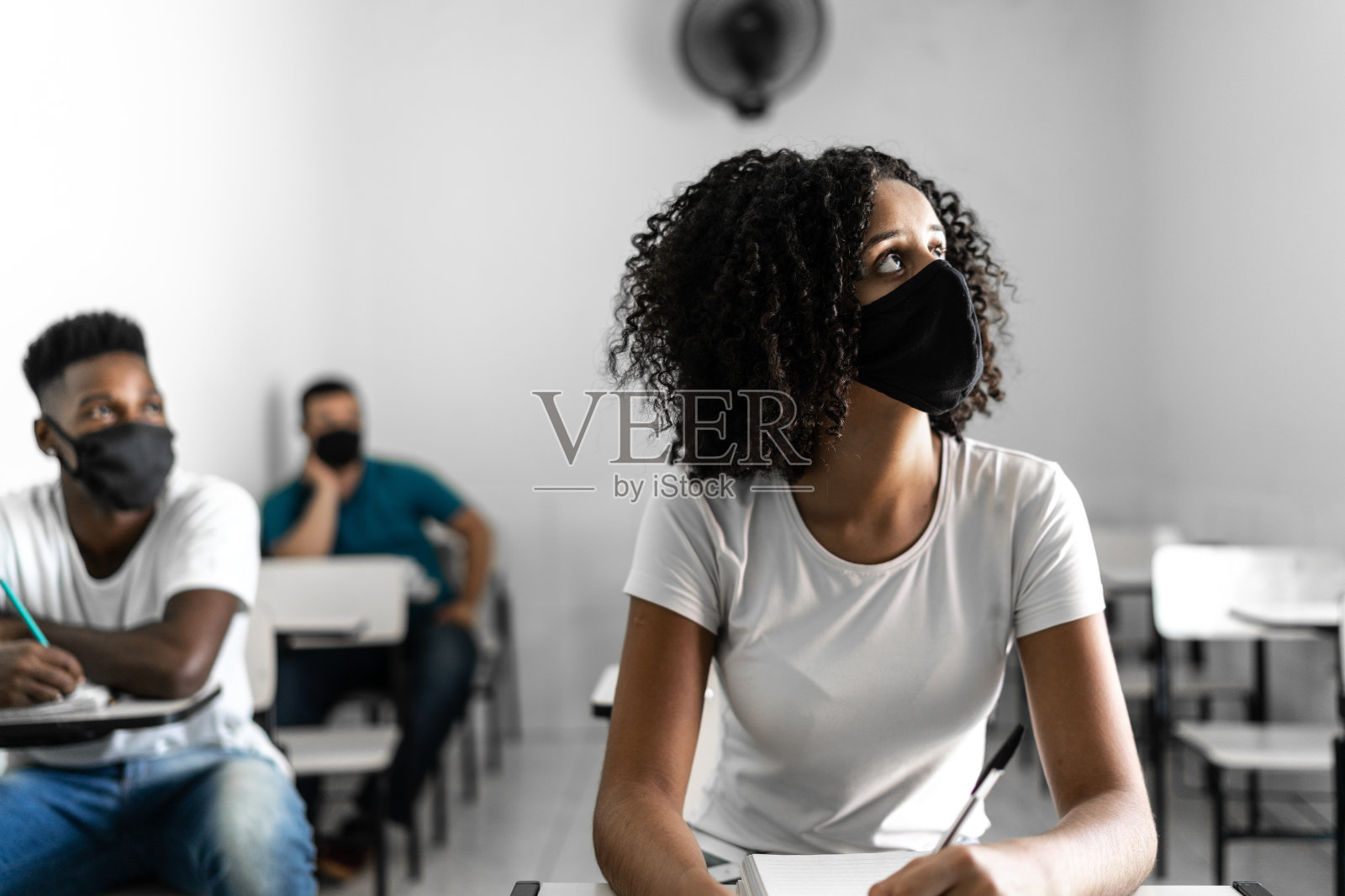 学生戴着口罩望向别处,在教室里沉思照片摄影图片