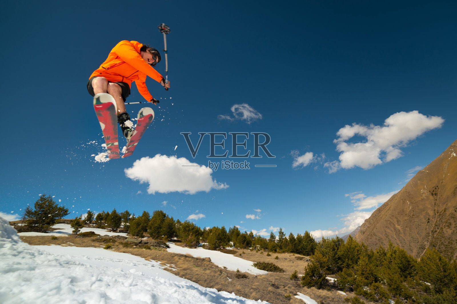 一名戴着太阳镜的年轻人在山的背景下用踢雪器玩飞行把戏照片摄影图片