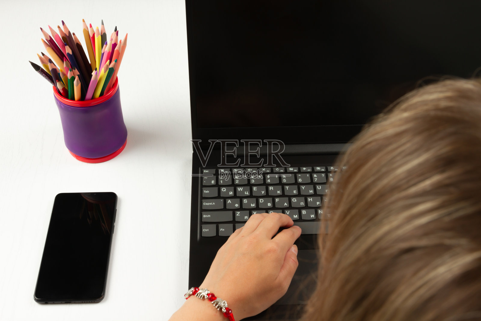 白色的木桌上放着一部智能手机和一台笔记本电脑,女性的手正在上面打字照片摄影图片