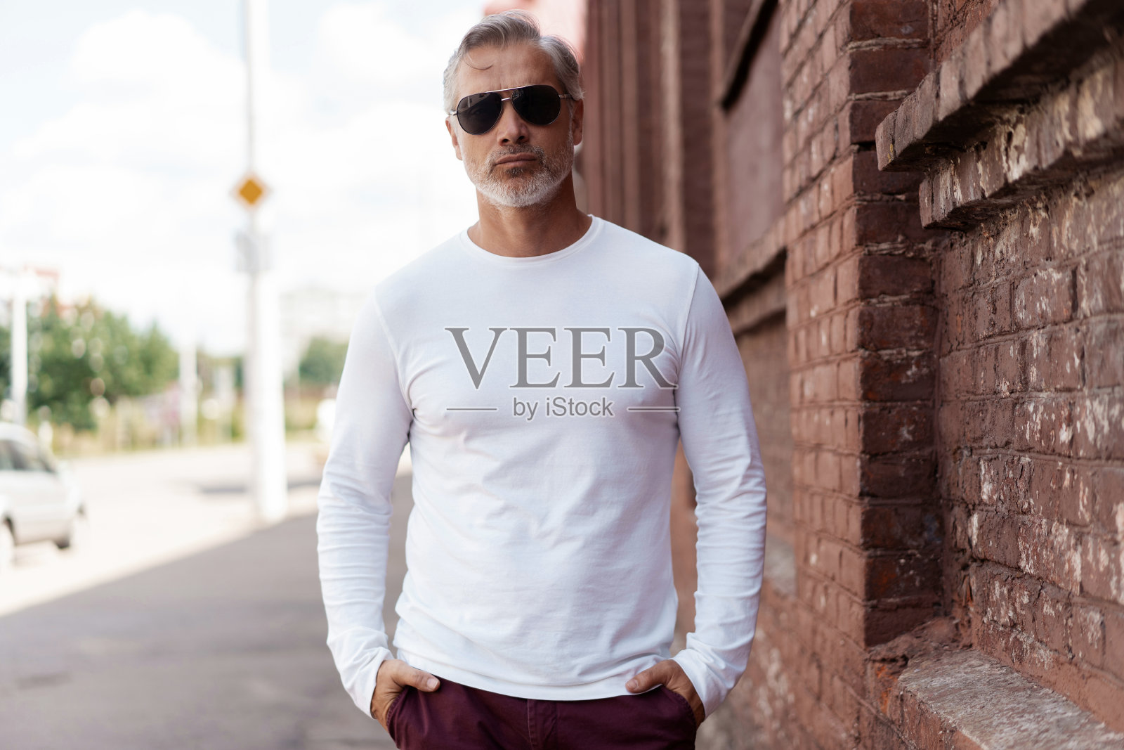 一个灰色头发的男人的肖像,穿着牛仔裤和白色t恤的成熟英俊的男人,斜靠在旧墙照片摄影图片