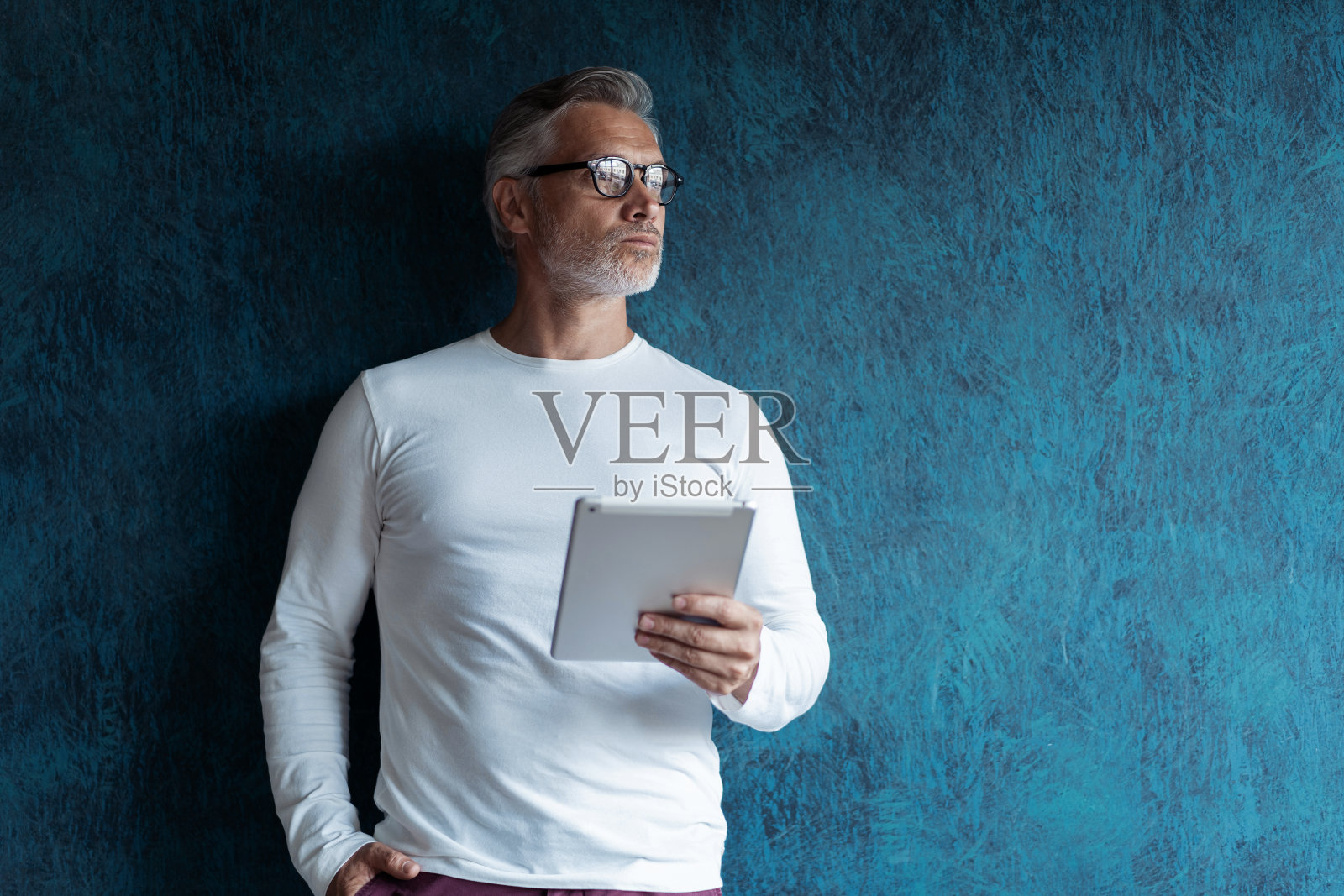 成熟男性高管在深蓝色背景下使用数码平板电脑。照片摄影图片