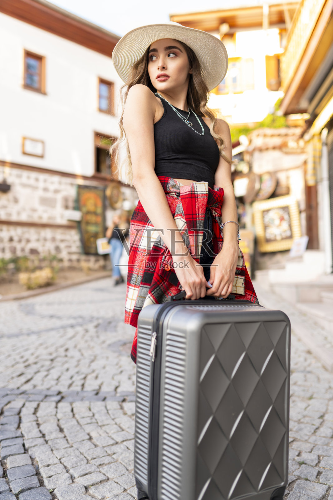 一个年轻的女性旅行者带着一个黄色的手提箱走在户外的现代交通站。城市交通和旅行的概念照片摄影图片