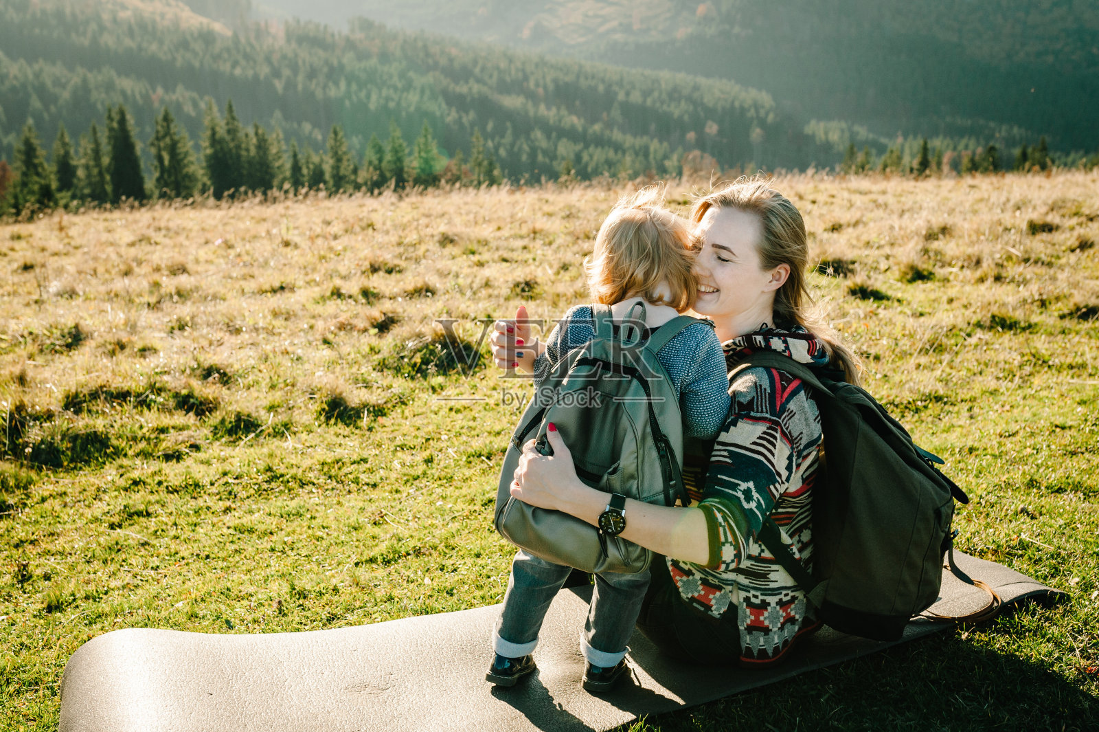 女儿拥抱父母的自然。妈妈背着双肩包和孩子走在秋天的草地上。家人一起在山外度假。旅行的概念。世界旅游日。照片摄影图片