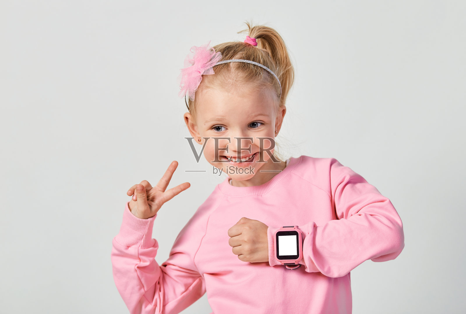 可爱的白人小女孩,4-5岁,手腕上戴着智能手表。针对儿童的科技,对抗灰色的工作室背景照片摄影图片