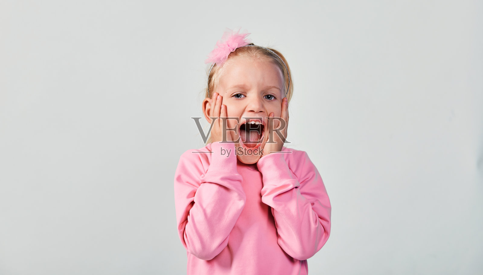 4-5岁的可爱女孩在工作室里穿着粉红色运动衫做出惊讶的脸照片摄影图片