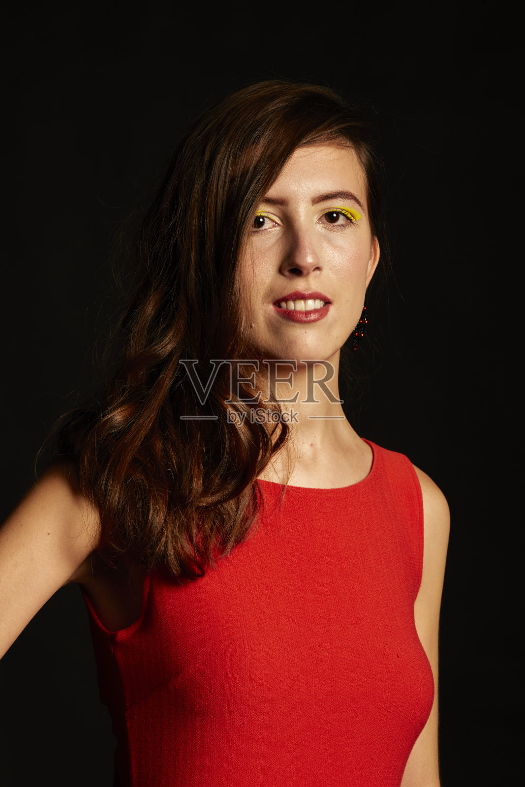 年轻的深色头发的西班牙女人穿着性感的红色连衣裙,搭配珍珠耳环,黑色的鞋子在黑色的背景照片摄影图片