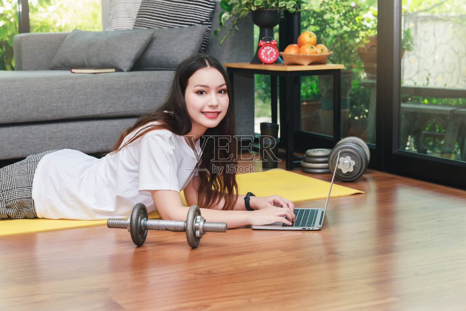 美丽的年轻女子在笔记本电脑上看在线健身视频教程,而躺在客厅的地板上。照片摄影图片