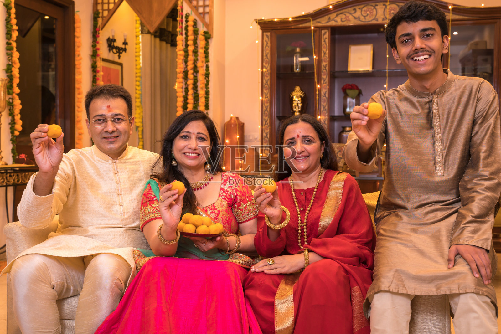 一家人穿着民族服装坐在沙发上向镜头展示mithai照片摄影图片