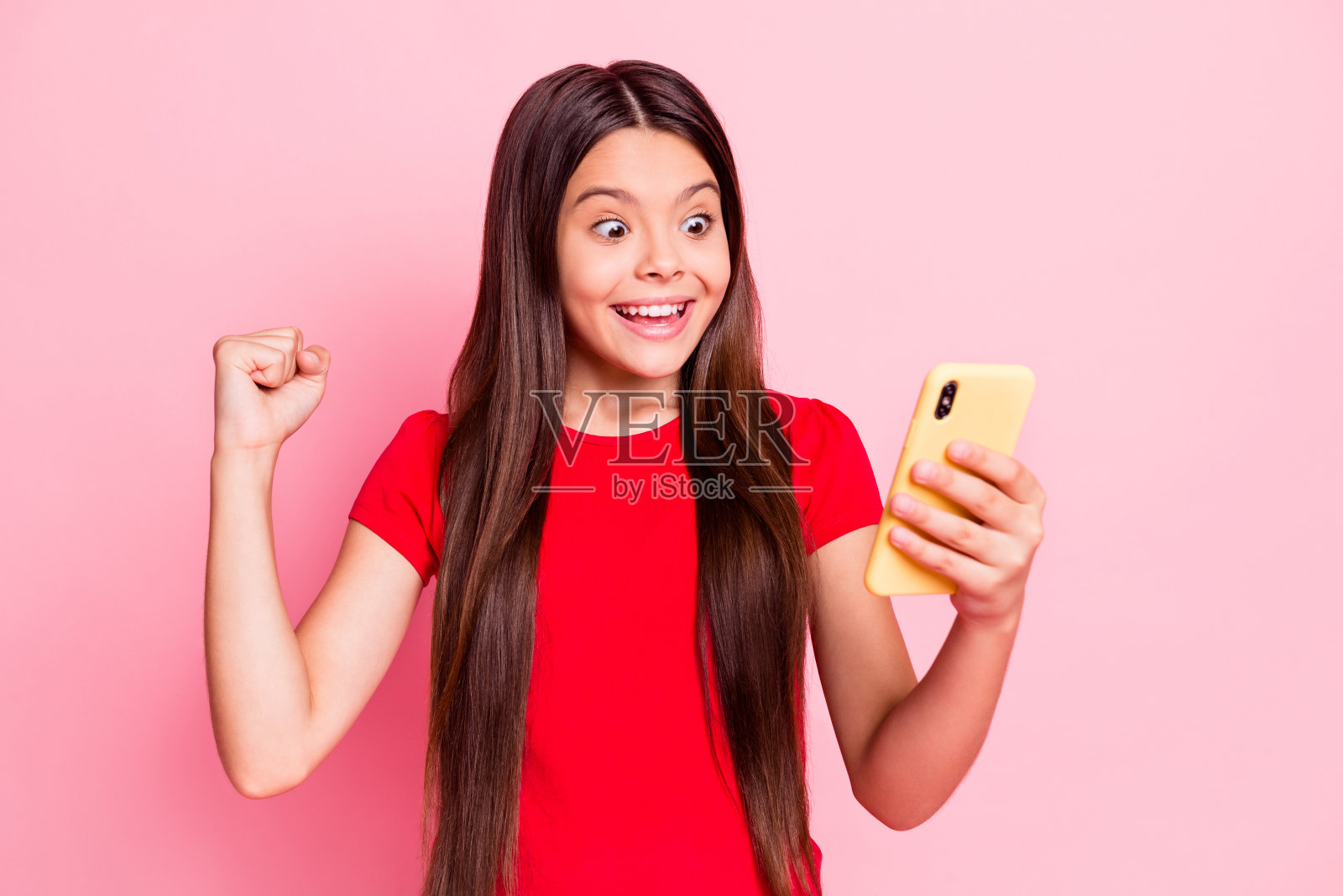 可爱可爱的照片小女士长头发,举起手,手臂,拳头,握电话,震惊,惊讶,兴奋,疯狂,惊讶,看穿休闲的红色t恤,孤立的粉红色背景照片摄影图片