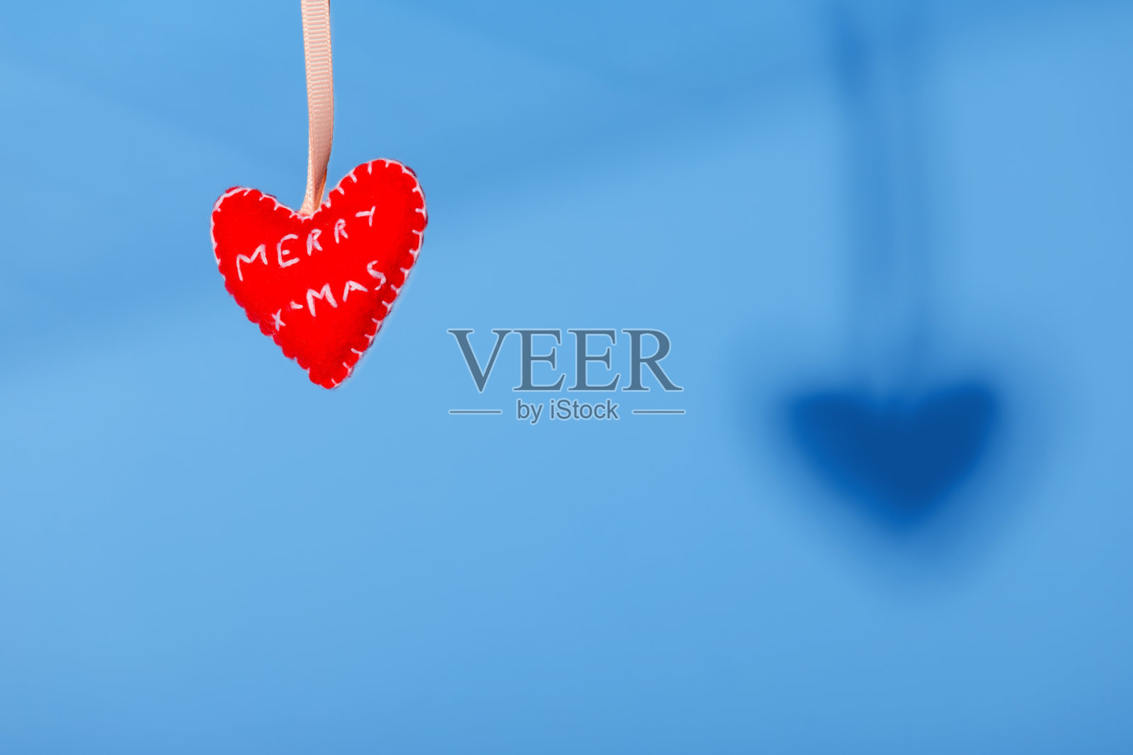 红色手工制作的心形圣诞玩具挂在蓝色的背景下。复制空间,最小照片摄影图片