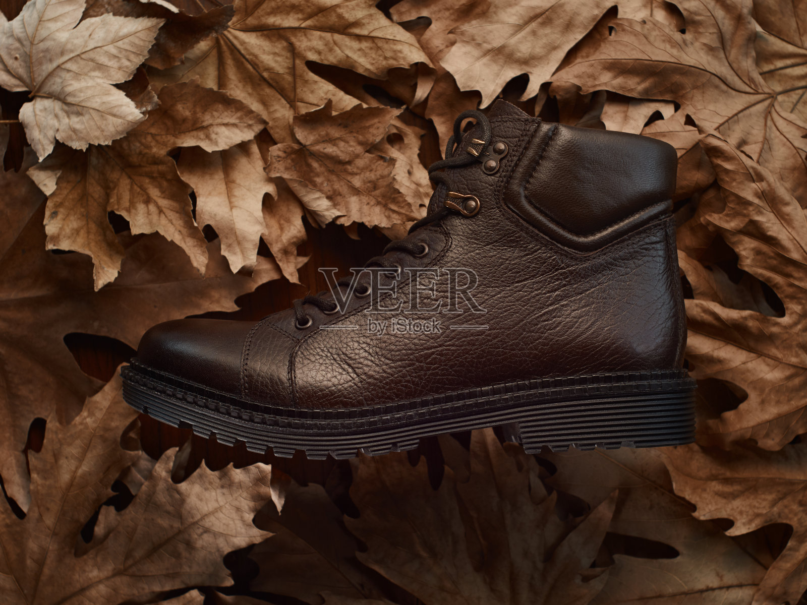 棕色男徒步靴上秋叶飘落,侧视照片摄影图片