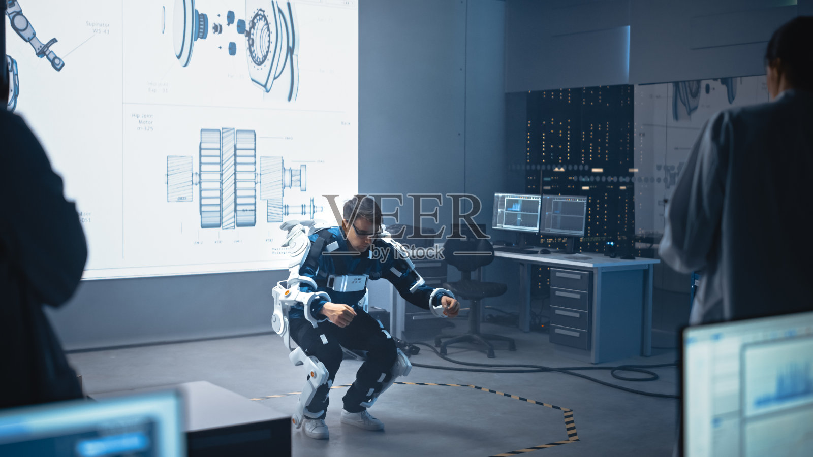 在开发实验室:工程师和科学家看机器人外骨骼原型演示与人测试它,做仰卧起坐。设计可穿戴Exosuit来帮助人们照片摄影图片