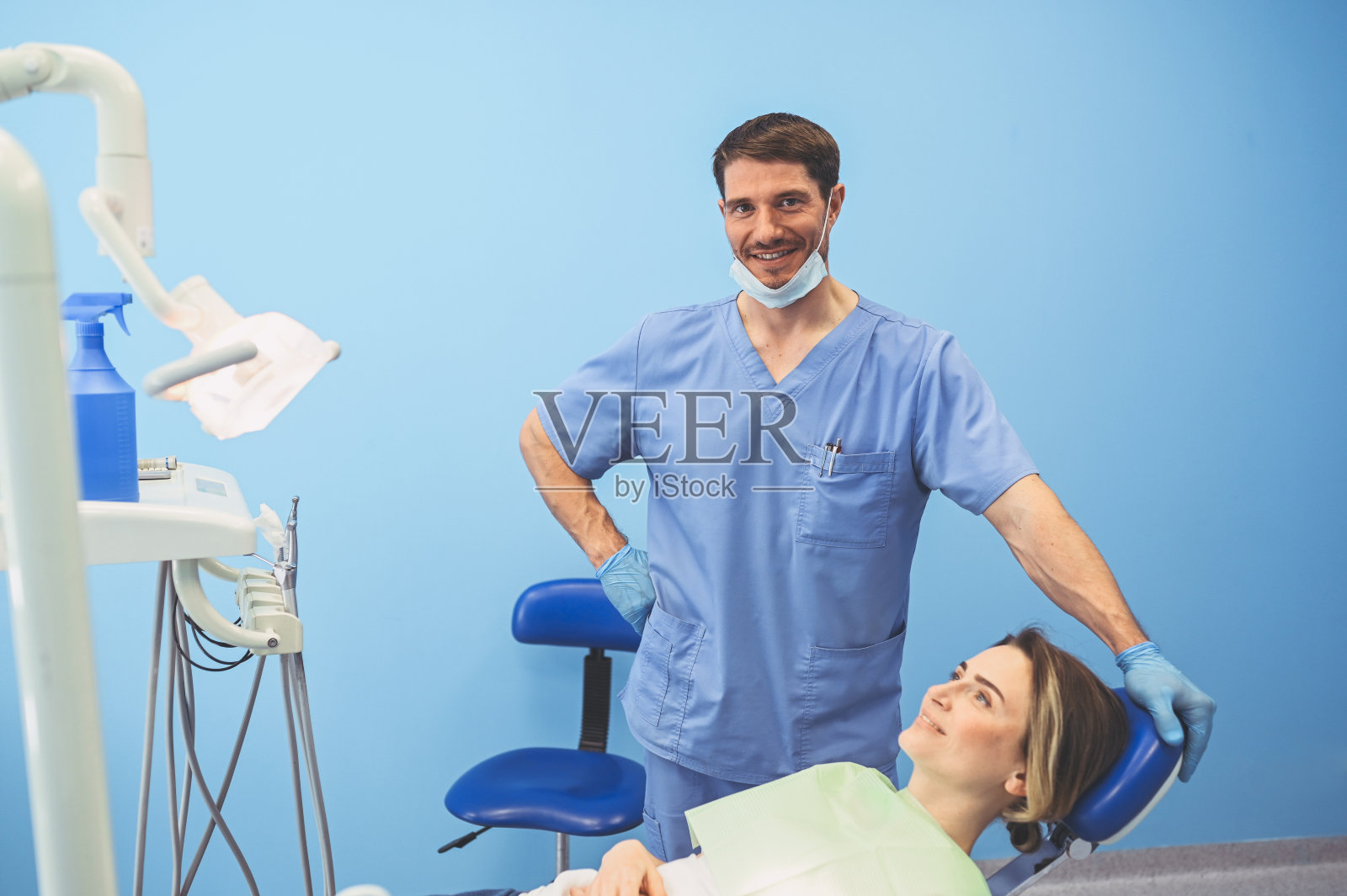 牙科医生在牙科诊所使用牙科设备检查病人的牙齿。口腔医学与健康理念。年轻英俊的男医生戴着一次性医用面膜,微笑着快乐的女人。照片摄影图片