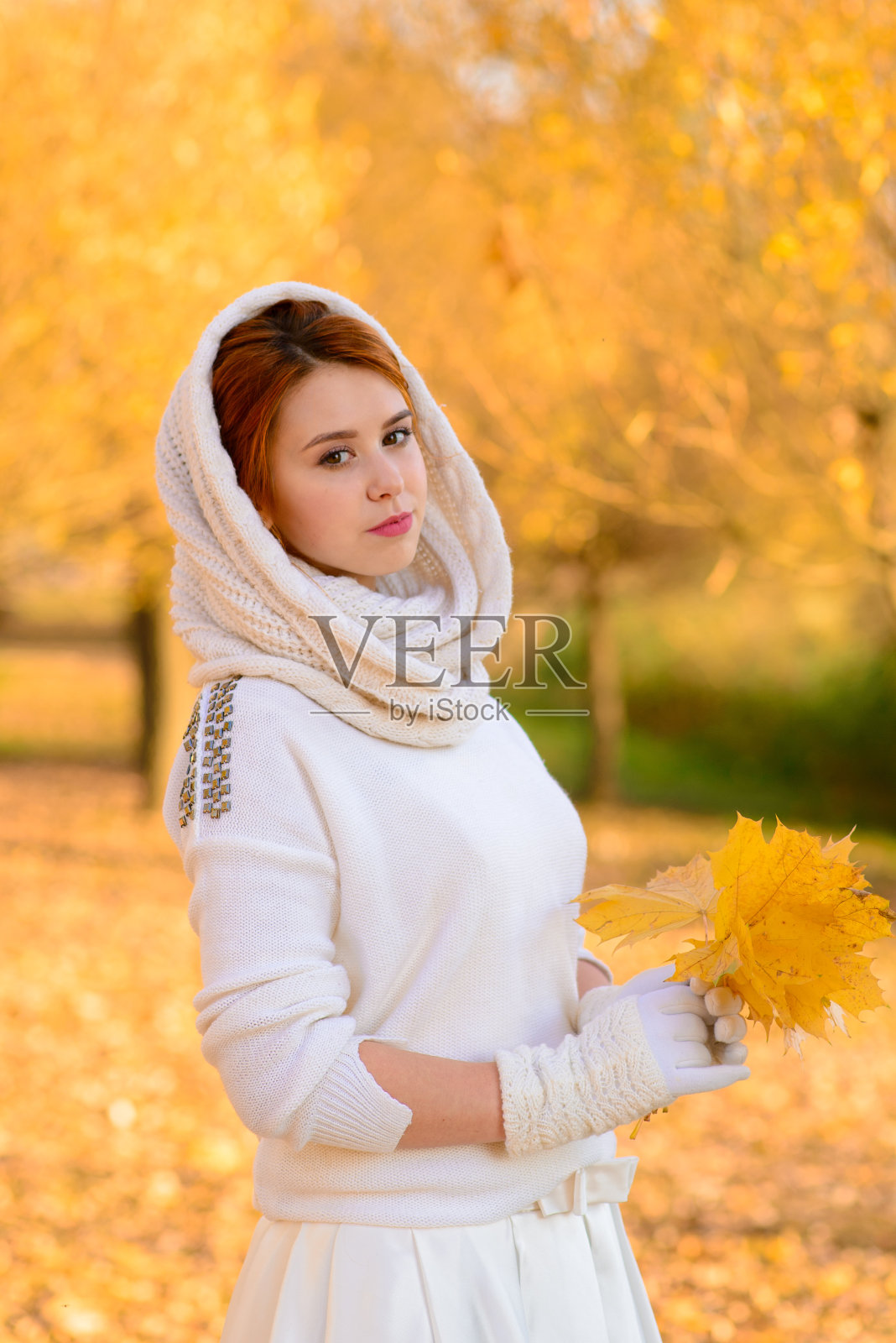 可爱的女孩在长长的白色婚纱摆姿势在秋天的树木之间的乡村小路在金色的时间气氛。照片摄影图片