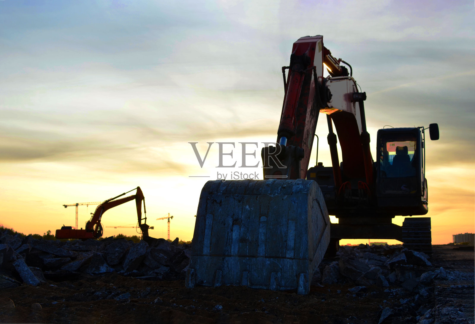 挖掘机对混凝土和坚硬岩石的破坏,在夕阳背景下的施工现场照片摄影图片