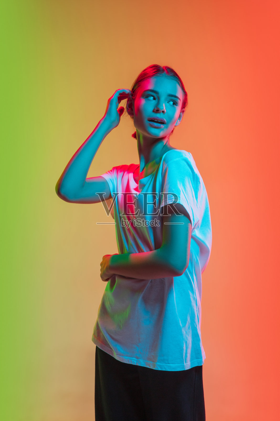 年轻的白人女孩的肖像在渐变的绿橙色工作室背景霓虹灯照片摄影图片