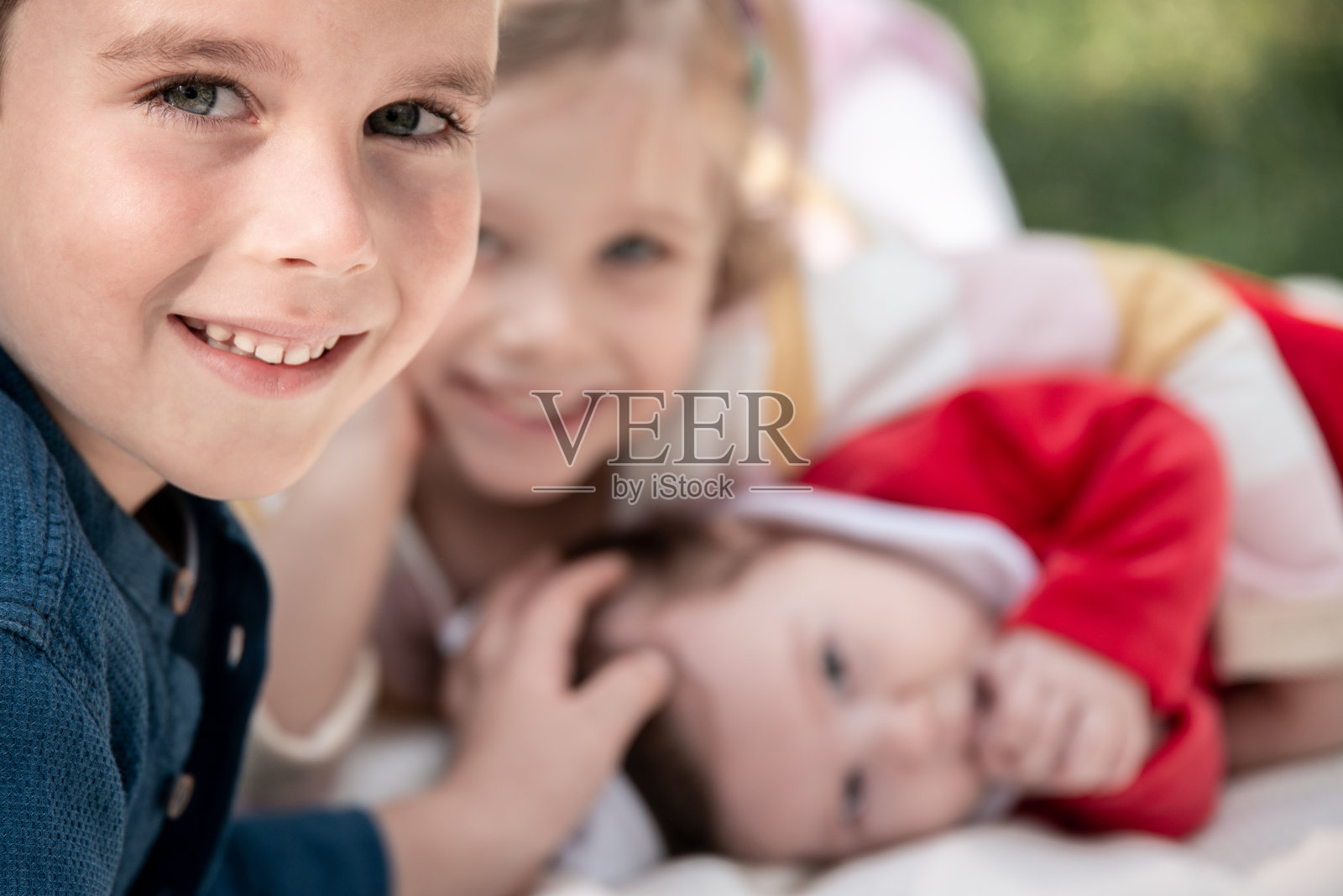 特写,三个孩子一起在花园野餐毯子上玩耍照片摄影图片