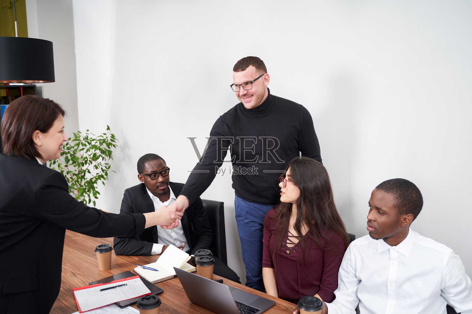 年轻快乐的商务人士在现代办公室一起工作,多民族团队合作。与握手问候照片摄影图片