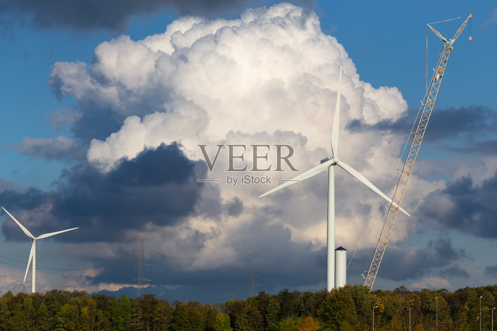 在一个戏剧性的多云的天空和森林的背景上建造一个风力发电机和电线照片摄影图片