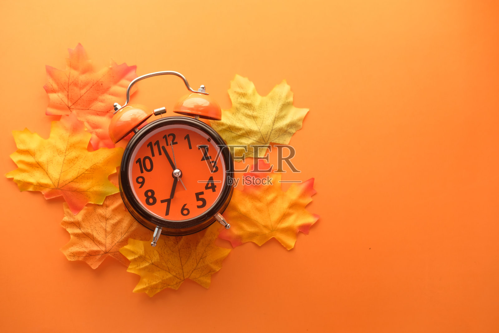 闹钟上的秋叶以橙色为背景照片摄影图片