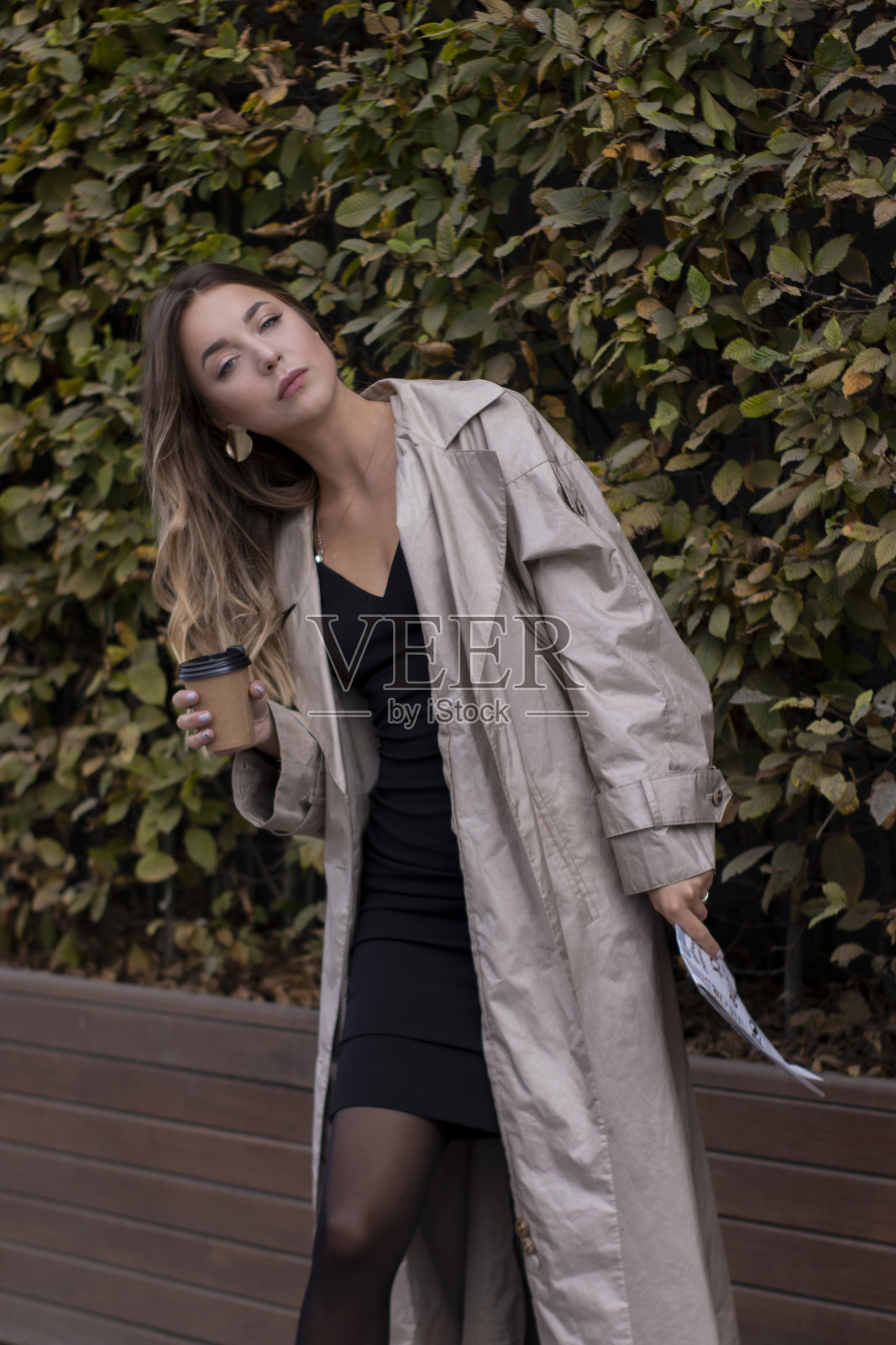 漂亮的年轻的黑发,穿着时尚的风衣和黑色连衣裙走过街道。秋天,黄色的叶子。照片摄影图片