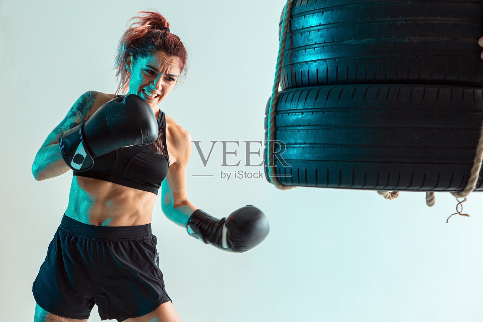 一个女拳击手在拳击手套打击轮胎与她的手照片摄影图片