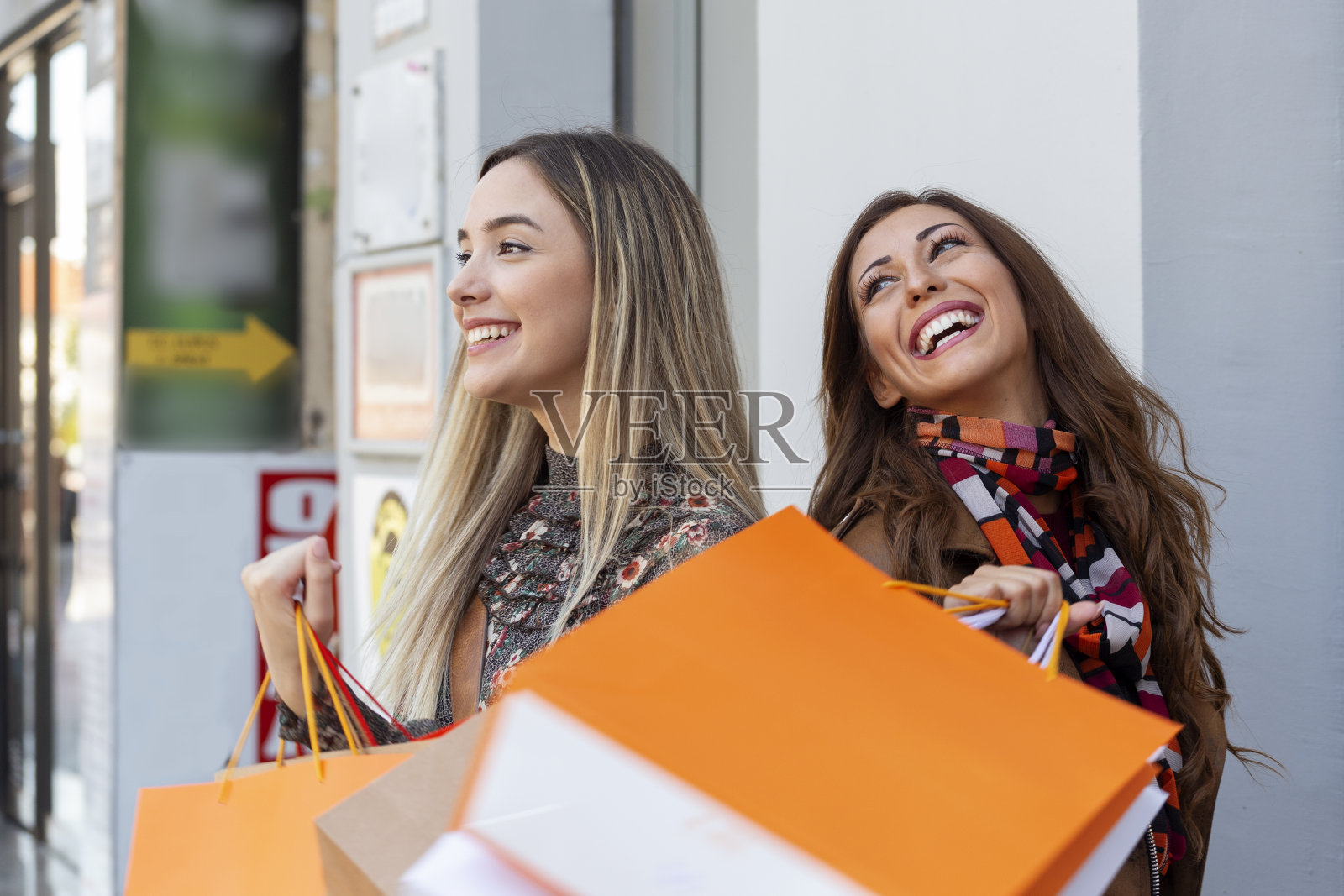 两个女人在街上的橱窗前购物,手里拿着包照片摄影图片