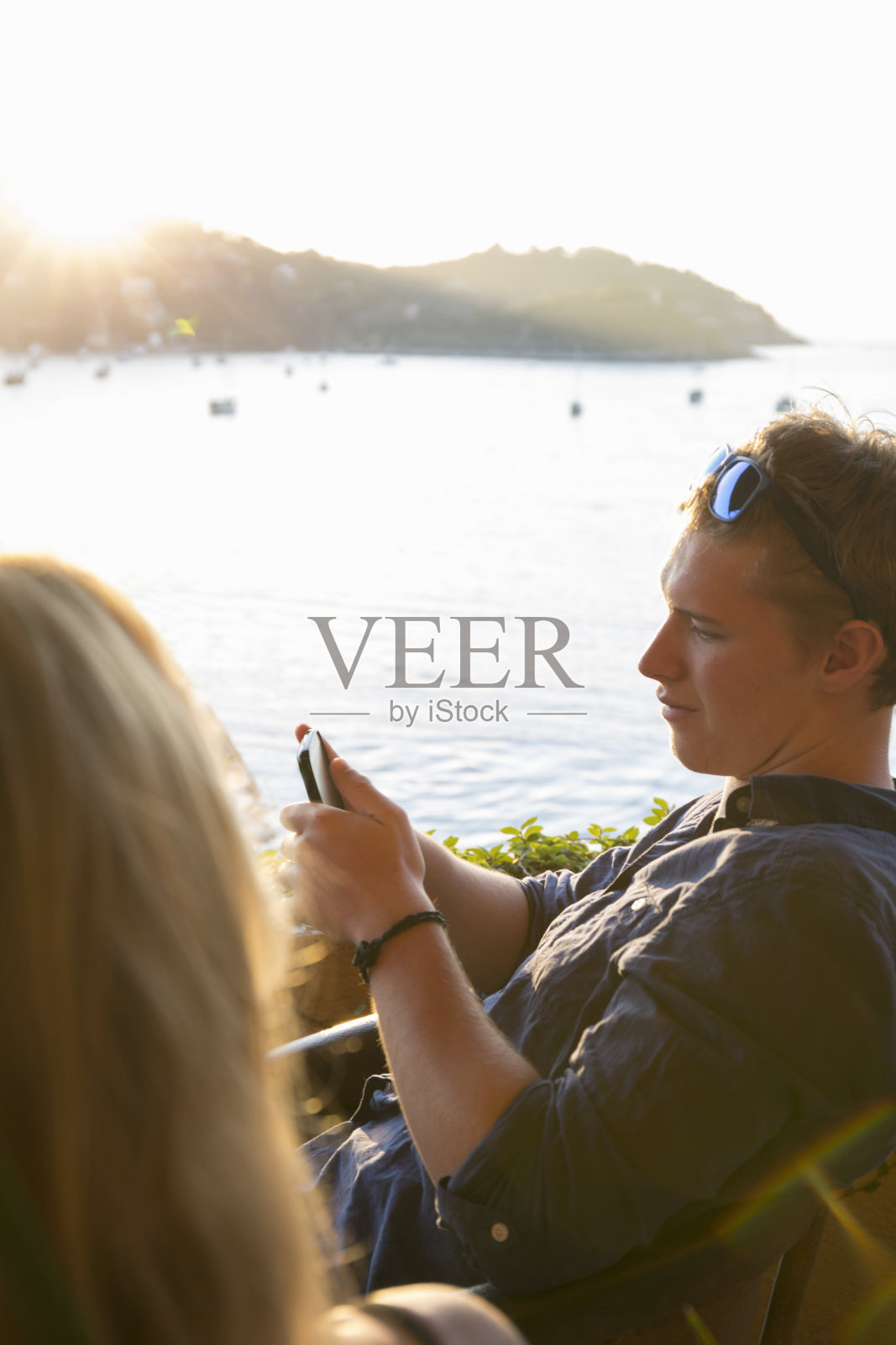 在日落时分用数码手机向年轻男子看过去的女子照片摄影图片