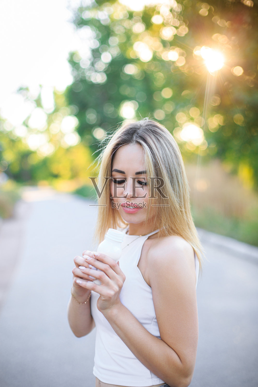 一个年轻的女人拿着一个小的瓶子在公园的小路上照片摄影图片