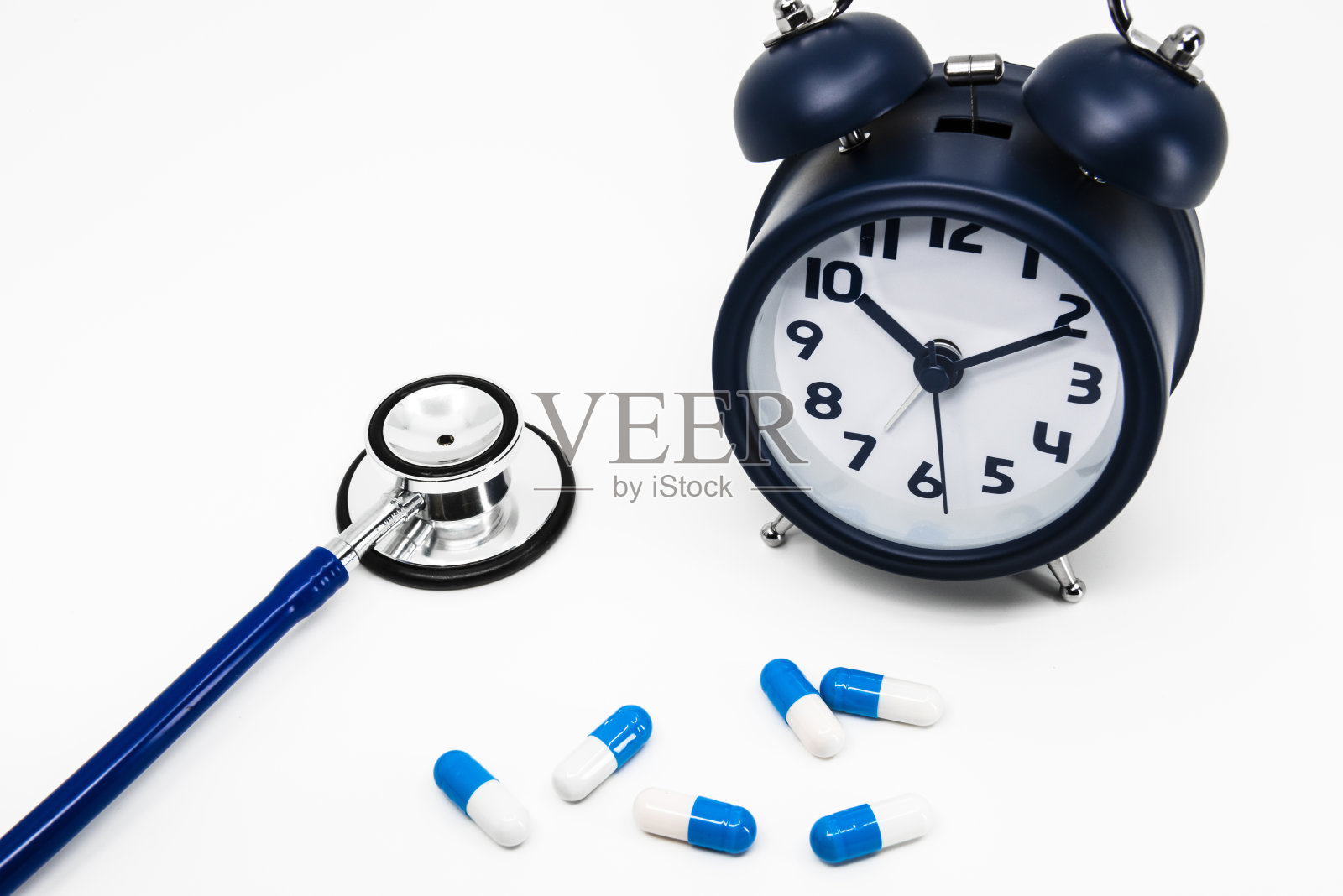 一个时钟,听诊器和蓝色胶囊药物在白色的背景照片摄影图片