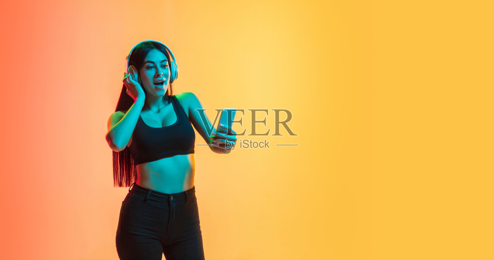 在霓虹灯下的黄橙色画室背景上,年轻女子的肖像照片摄影图片