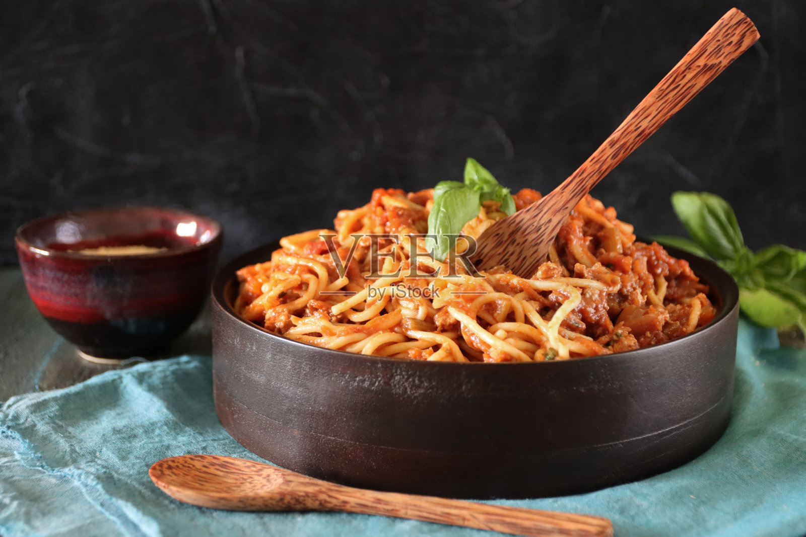 这是一幅意大利面与自制的肉酱、浓番茄酱、洋葱、大蒜和罗勒叶配菜混合在一起的画面,用木器盛在黑色的碗里照片摄影图片