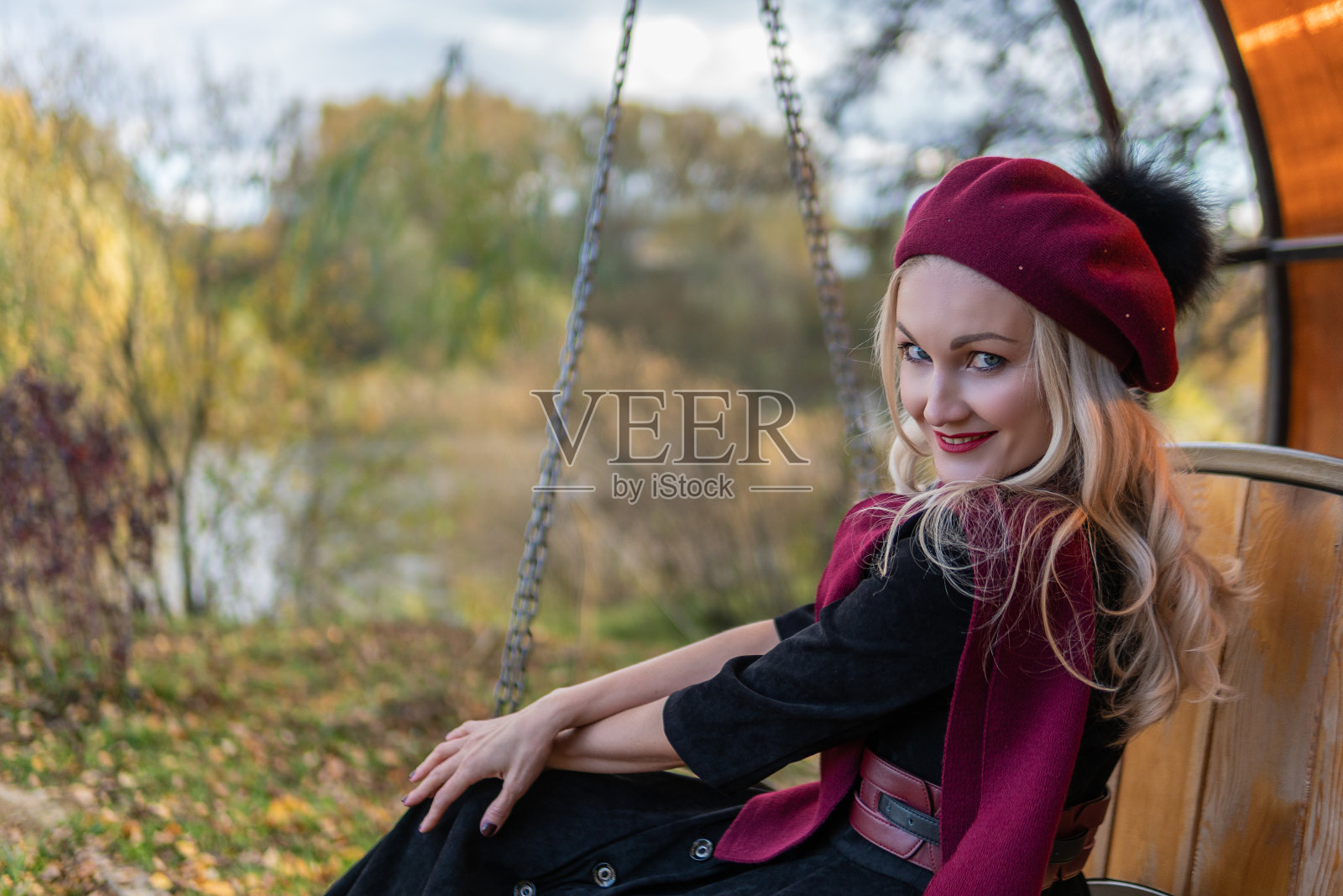 一个女孩坐在花园里的秋千上,身穿勃艮第外套和短上衣,在树木和蓝天的映衬下,有着魅力四射的外表。照片摄影图片